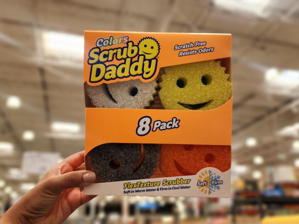 The writer holds an orange box of eight yellow, white, black, and red Scrub Daddy sponges