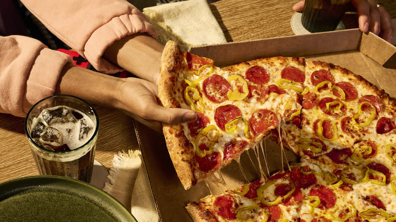 Person taking a slice from a box of pizza