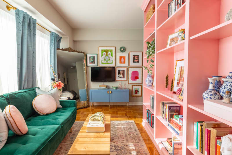 A living room with a green fabric couch across from a pink bookcase and gallery wall