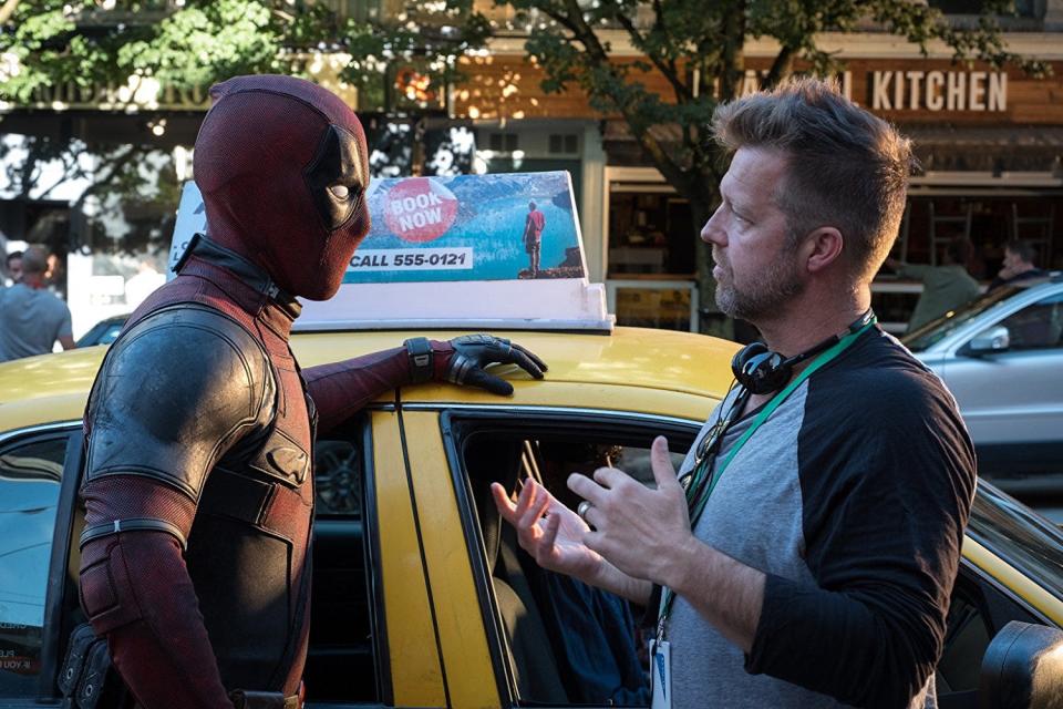Deadpool standing next to David Leitch by a taxi cab