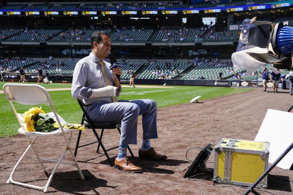 Los Angeles Dodgers television reporter David Vassegh works on a pregame broadcast before a baseball game against the Milwaukee Brewers Thursday, Aug. 18, 2022, in Milwaukee. Vassegh said he broke two bones in his right wrist and cracked six ribs Wednesday when he tumbled and crashed into the padding at the end of his slide down "Bernie's Chalet," where Brewers mascot Bernie Brewer takes up residence behind the American Family Field left-field stands. (AP Photo/Morry Gash)