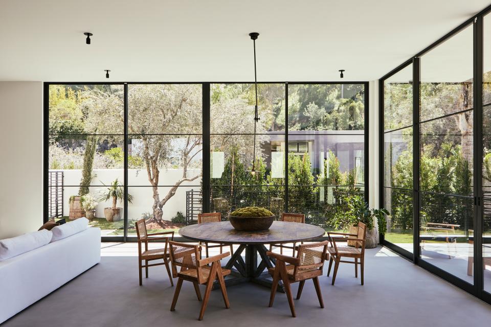 In the dining room, the vintage industrial O.C. White ceiling pendant from 1stdibs hangs above the cerused/limed oak Belgian dining table from Lucca Antiques surrounded by Pierre Jeanneret cane chairs.