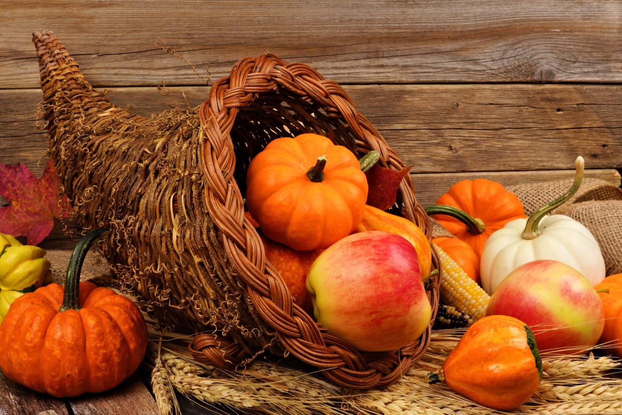 Thanksgiving cornucopia filled with pumpkins and fruit against a rustic wooden background.