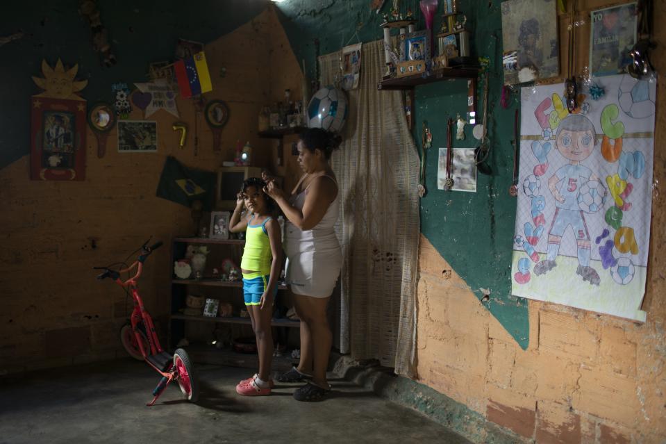 Yangervis Blanco, 7, stands still as her mother helps her prepare for a homespun beauty pageant in the Antimano neighborhood of Caracas, Venezuela, Friday, Feb. 5, 2021. Neighbors in the hillside barrio gathered for the carnival pageant tradition to select their child queen for the upcoming festivities. (AP Photo/Ariana Cubillos)