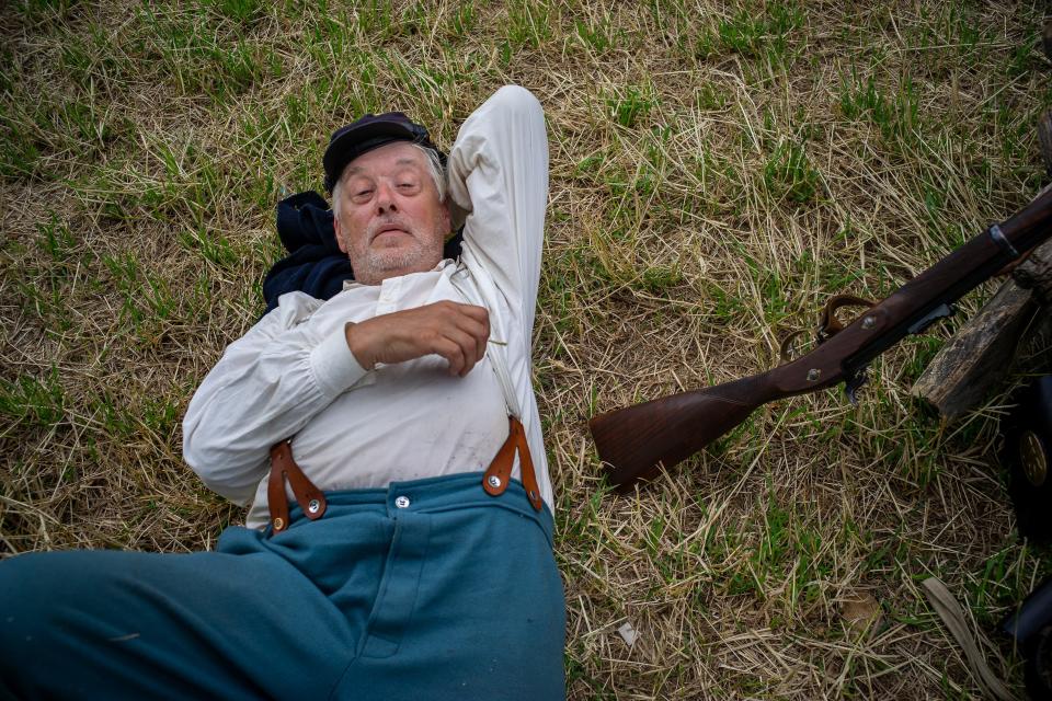 A man lies in the grass with a long rifle at his side.