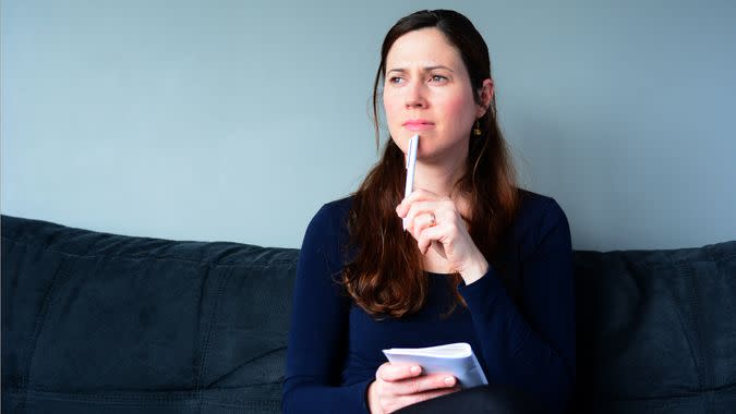 Young woman in her thirties (30s) hold a notepad thinking about to do list at home.