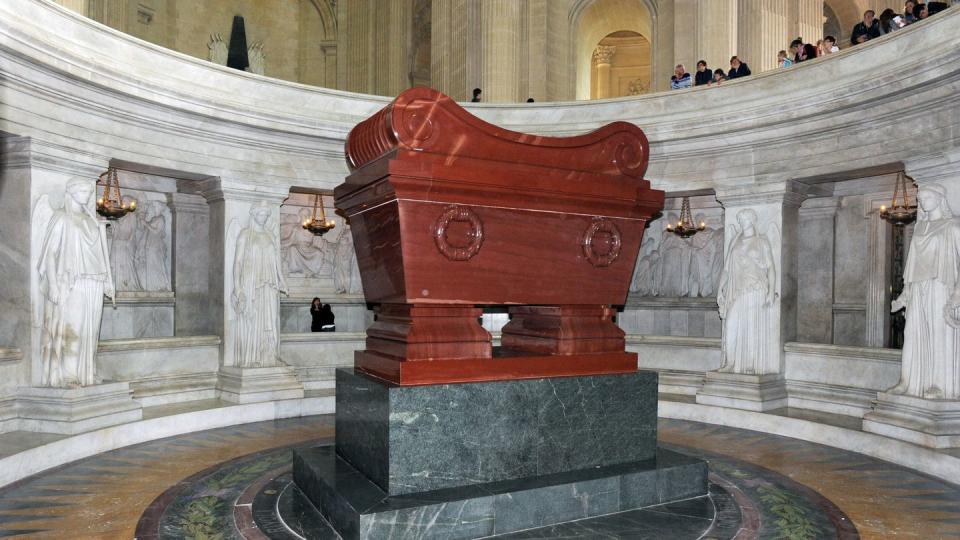 a large coffin rests in a viewing area with tourists looking on