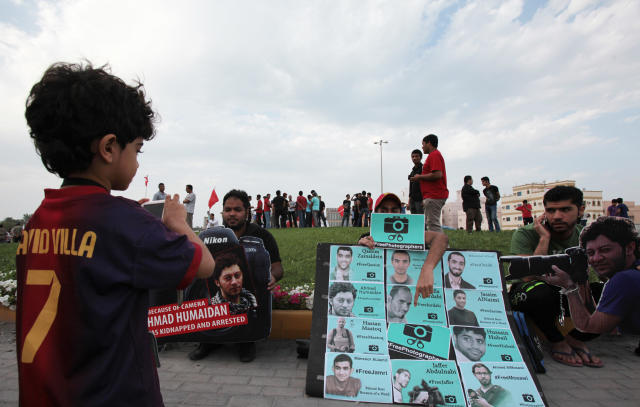 In this photo taken Friday, March 21, 2014, a Bahraini boy takes pictures of a protest in support of jailed photographers, including Ahmed Humaidan, seen in a cutout at right, during a march in Abu Saiba, west of the capital, Manama, Bahrain. A defense lawyer said Wednesday that a court in Bahrain has given 28 people, among them a photojournalist, prison sentences of up to 10 years on charges of attacking a police station and vandalism during protests. (AP Photo/Hasan Jamali)