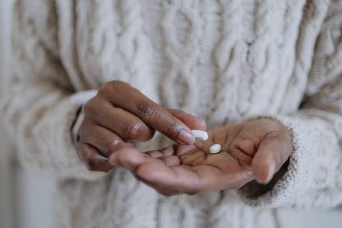 A person is holding two white pills in their hand, wearing a textured sweater