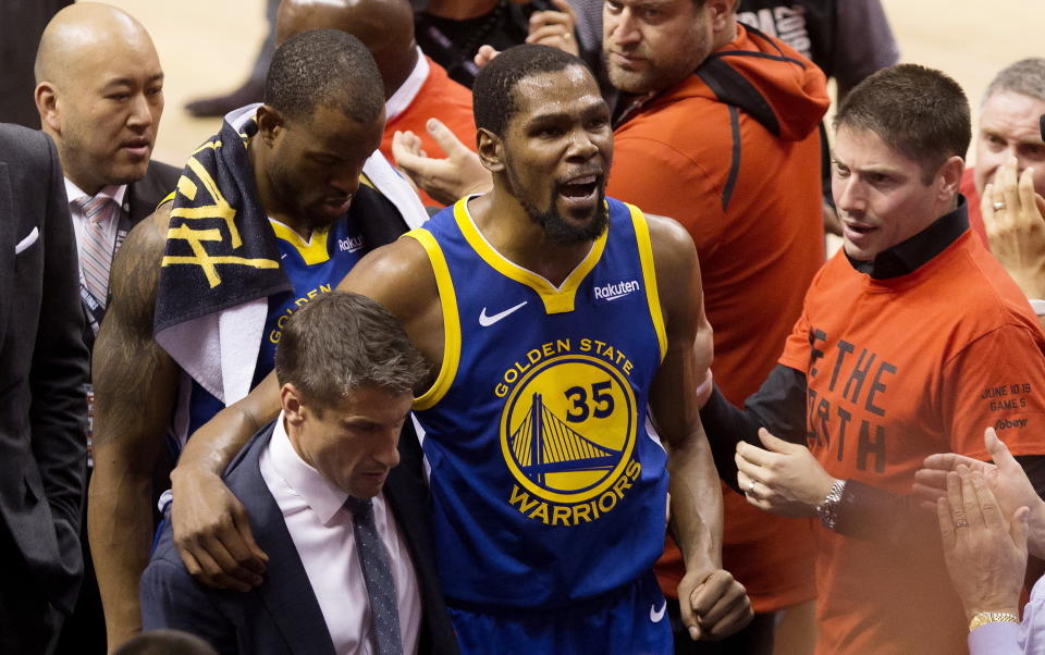 Kevin Durant, alero de los Warriors de Golden State, es ayudado a salir de la cancha tras lesionarse durante el quinto partido de la Final de la NBA ante los Raptors de Toronto, el lunes 10 de junio de 2019 (Chris Young/The Canadian Press via AP)