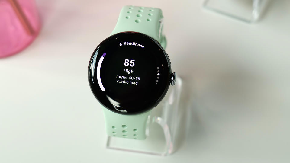 A Pixel Watch 3 with a green band on a stand. Its screen shows the Readiness page with a score of 85. Words below indicate this is a high score and that the Target Cardio Load is 40-55.