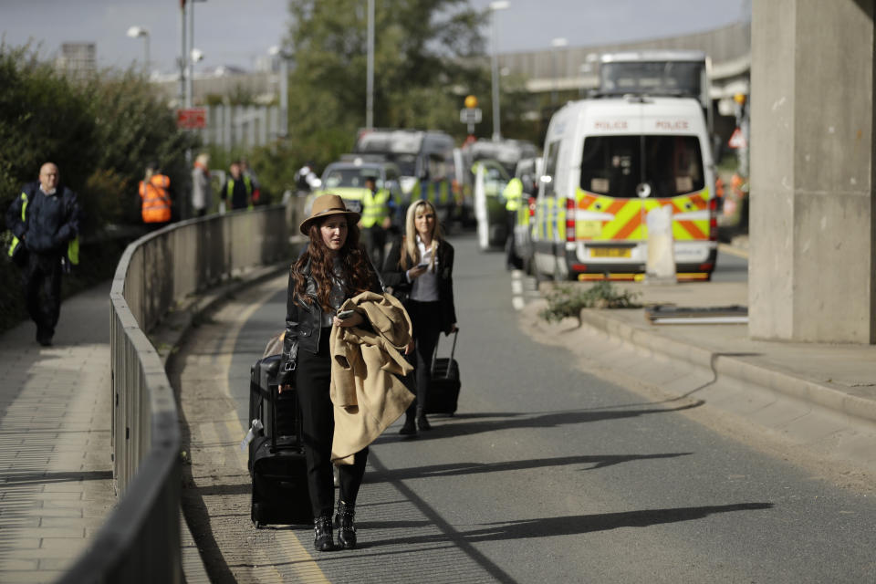 Passengers arrive on foot from a traffic jam caused by Extinction Rebellion climate change protesters blocking a road outside City Airport in London, Thursday, Oct. 10, 2019. Some hundreds of climate change activists are in London during a fourth day of world protests by the Extinction Rebellion movement to demand more urgent actions to counter global warming. (AP Photo/Matt Dunham)