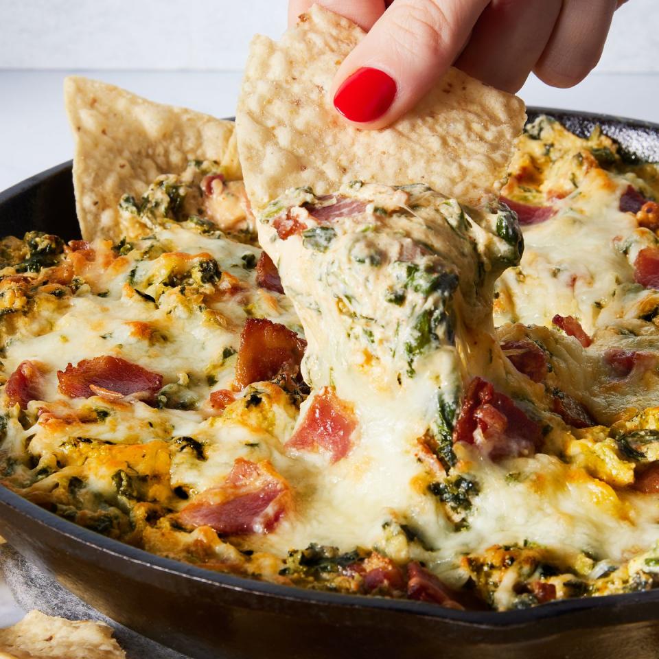 spinach dip in a cast iron skillet with bacon served with chips