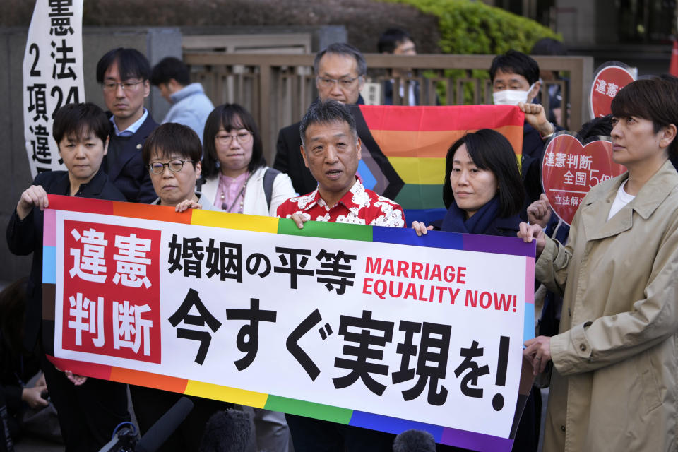 One of the plaintiffs, in a red and white shirt, center, speaks in front of media members by the main entrance of the Tokyo district court after hearing the ruling regarding LGBTQ+ marriage rights, in Tokyo, Thursday, March 14, 2024. The banner reads: "Marriage Equality (upper) and Fulfill it right now! (lower)". (AP Photo/Hiro Komae)