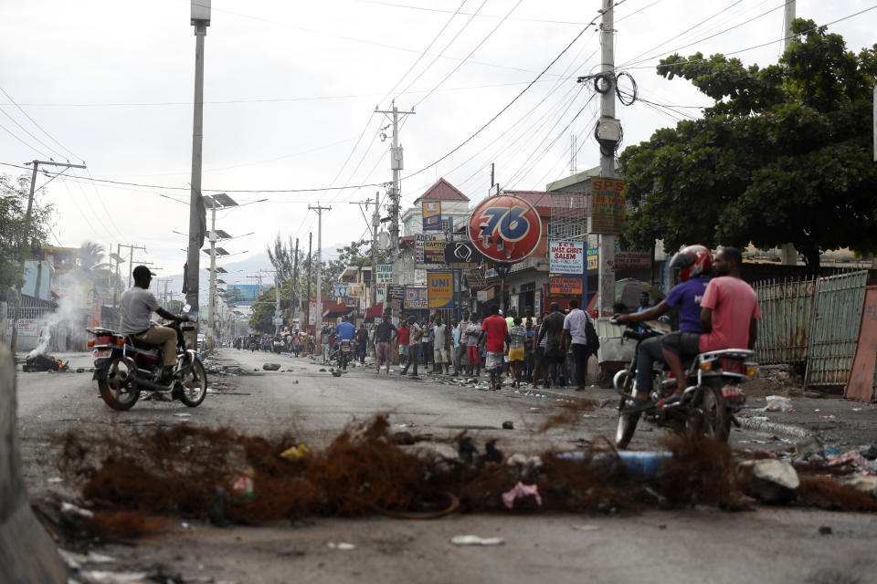 Motorcyclists ride around a barricade set up by protesters in Port-au-Prince, Haiti, Monday, Sept. 30, 2019. Opposition leaders are calling for a nationwide push Monday to block streets and paralyze Haiti's economy as they press for Moise to give up power, and tens of thousands of their young supporters were expected to heed the call. (AP Photo/Rebecca Blackwell)