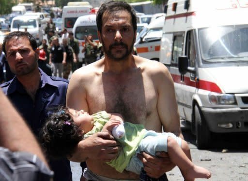 A Syrian man carries a wounded girl next to following an explosion that targeted a military bus near the Qudssaya neighbourhood in the Syrian capital Damascus. UN monitors have finally reached the site of a new massacre in Syria at a second attempt, activists said, as Western powers pressed at the United Nations for sanctions against Damascus