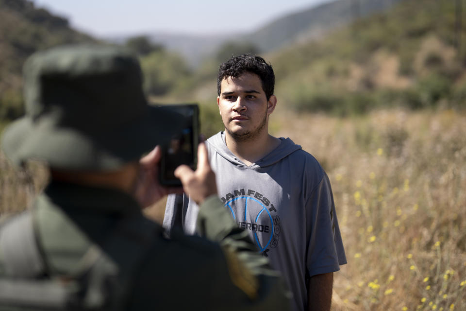 A migrant seeking asylum stands as a Border Patrol agent takes his picture before being transported and processed, Wednesday, June 5, 2024, near Dulzura, Calif. President Joe Biden on Tuesday unveiled plans to enact immediate significant restrictions on migrants seeking asylum at the U.S.-Mexico border as the White House tries to neutralize immigration as a political liability ahead of the November elections. (AP Photo/Gregory Bull)