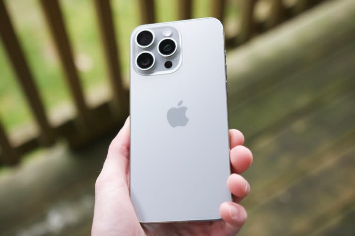 Someone holding an iPhone 15 Pro Max outside on a patio, showing the back of the Natural Titanium color.