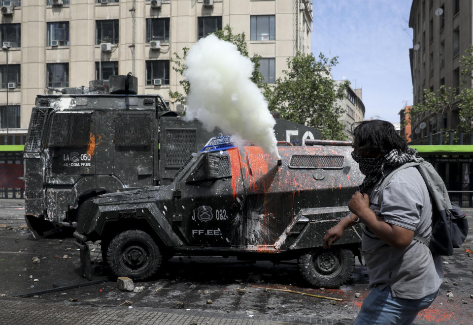 A demonstrator throws stones at a police armored vehicle spewing tear gas, during clashes in Santiago, Chile, Wednesday, Oct. 23, 2019. Rioting, arson attacks and violent clashes wracked Chile as the government raised the death toll in an upheaval that has almost paralyzed the South American country long seen as the region's oasis of stability. (AP Photo/Rodrigo Abd)