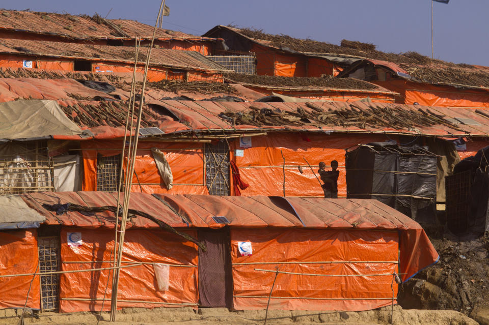 FILE - In this Sunday, Jan. 28, 2018, file photo, a Rohingya girl holds her brother while standing in front of their makeshift shelter at Jamtoli refugee camp in Cox's Bazar, Bangladesh. Authorities in Bangladesh said Tuesday, Oct. 22, 2019, that they want to start relocating thousands of Rohingya refugees to a Bay of Bengal island soon from crammed camps near the border with Myanmar, from where they fled. Top government administrator in Cox's Bazar, Kamal Hossain, said they listed 100 families willing to move to Bhasan Char, an island hours by boat from the mainland. The government has said it will relocate 100,000 refugees to the island in phases. (AP Photo/Manish Swarup, File)