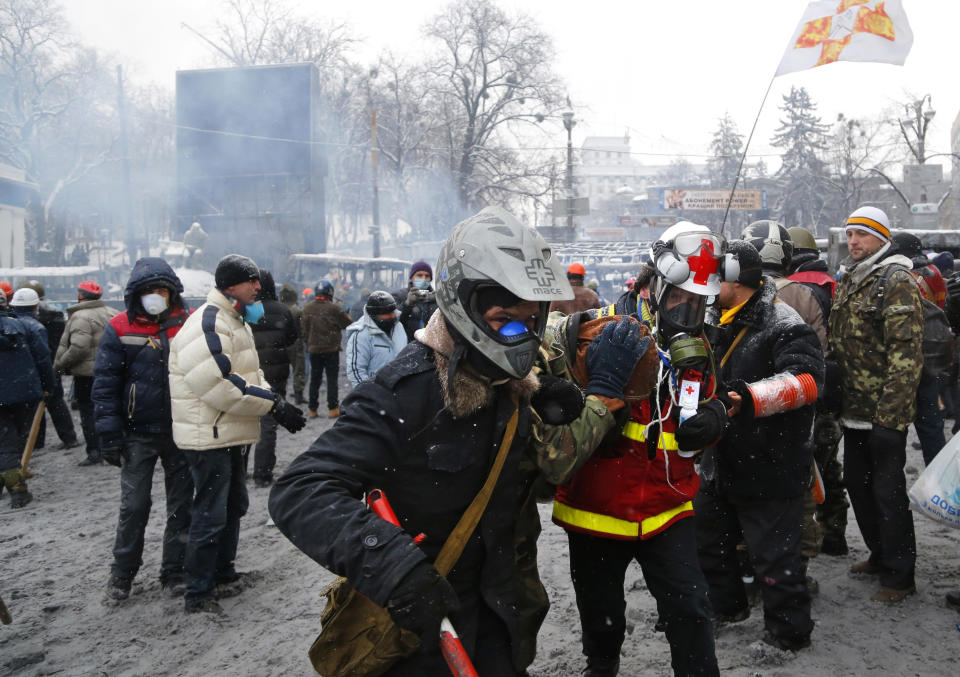 A wounded protester, foreground left, is assisted by a paramedic and fellow protester to go out during a clash with police in central Kiev, Ukraine, early Wednesday, Jan. 22, 2014. Two people have died in clashes between protesters and police in the Ukrainian capital Wednesday, according to medics on the site, in a development that will likely escalate Ukraine's two month-long political crisis. (AP Photo/Sergei Grits)