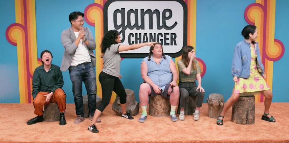 The contestants on "Game Changer: Battle Royale," reacting to a surprise judge announcement. From the left: Ally Beardsley, sitting on a log and yelling, Tao Yang standing with his hands clapped together, Rekha Shankar standing and pointing, Jacob Wysocki leaning back in shock, Vic Michaelis sitting with their hand over their mouth, and Lily Du standing and smile in a pose. 