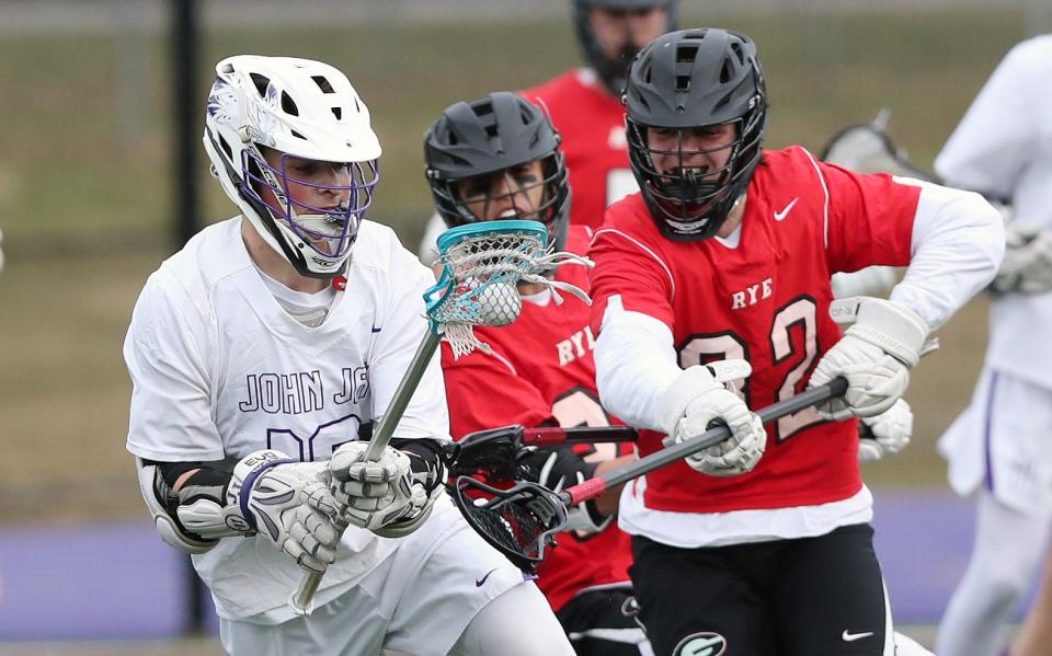 John Jay's Luke Mercer (19) drives to the goal in front of Rye's Brendan Lavelle (32) during boys lacrosse action at John Jay High School in Cross River March 29, 2019. John Jay won the game 8-6.