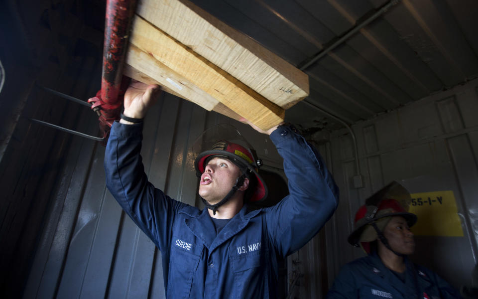 MRFN Benito Gueche, from the USS New York, pound wooden bits into a ruptured pipe that was flooding a compartment on a mock ship to stop the flooding during the Resolve Damage Control Olympics during Fleet Week in Fort Lauderdale, Fla., Tuesday, April 29, 2014. Three teams from the US Navy and Coast Guard ran drills that they would perform during an emergency on a ship. (AP Photo/J Pat Carter)