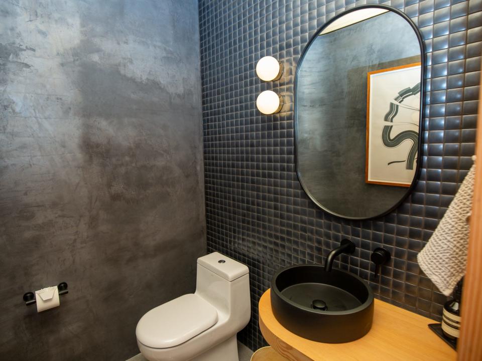 A bathroom with a toilet, mirror, and sink. The room has dark accents.