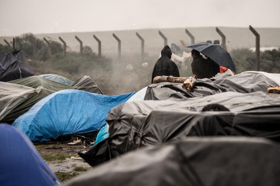 Illegal migrant stand on October 29, 2014 near makeshift tents in the northeastern French port of Calais. The mayor of Calais told lawmakers in London on October 28 that fencing donated by Britain to keep illegal migrants from the French exit port was "laughable" and said the border controls should be in Britain. Speaking to a British parliamentary committee, Natacha Bouchart also said it was easier to get welfare benefits in Britain and that migrants viewed the country as an "Eldorado".  Up to 2,300 migrants are thought to be in Calais and surrounding areas, overwhelming security forces as they make regular attempts to mob the port en masse to try and scramble onto trucks boarding ferries to the British port of Dover.      AFP PHOTO / PHILIPPE HUGUEN        (Photo credit should read PHILIPPE HUGUEN/AFP via Getty Images)