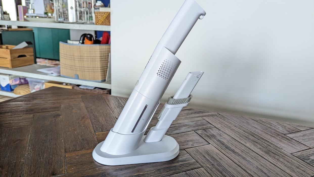 A white acerpure clean Lite compact vacuum cleaner with its stand on a brown wooden table.