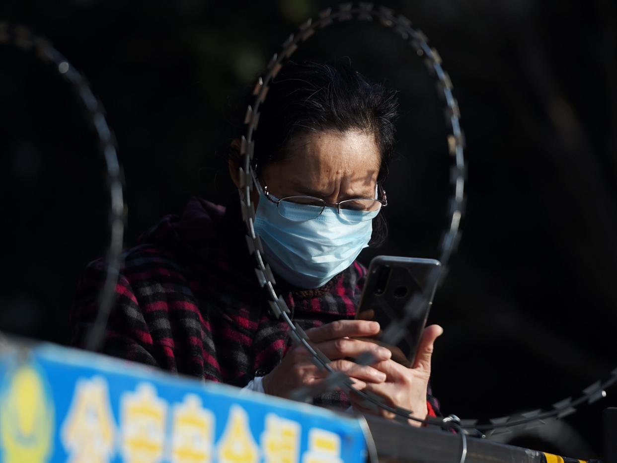 FILE PHOTO: A woman uses her mobile phone behind barbed wire at an entrance of a residential compound in Wuhan, the epicentre of the novel coronavirus outbreak, Hubei province, China February 22, 2020. REUTERS/Stringer/File Photo