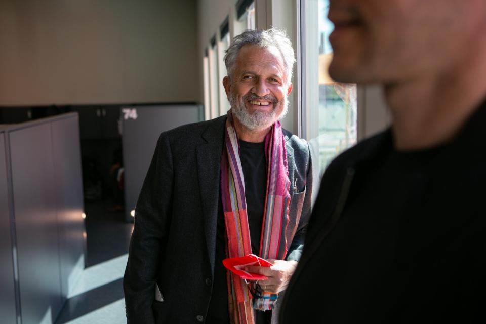 Architect Michael Lehrer, wearing a dark suit and red scarf, stands next to a window