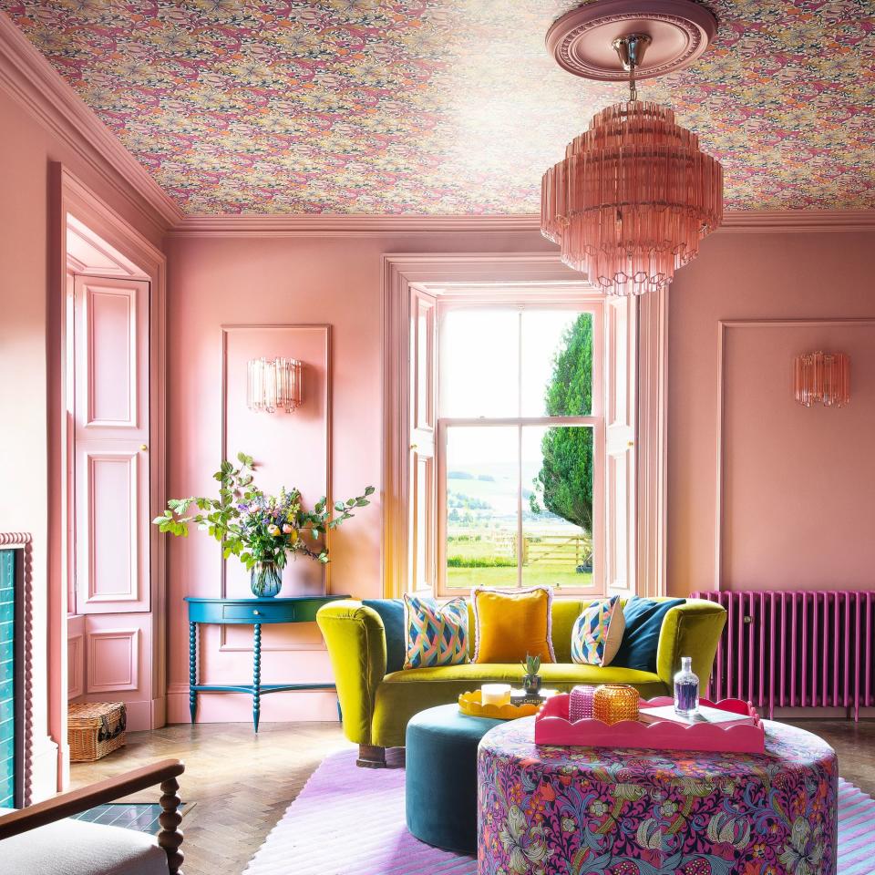 pink living room with patterned pouffe, yellow sofa and wallpapered ceiling