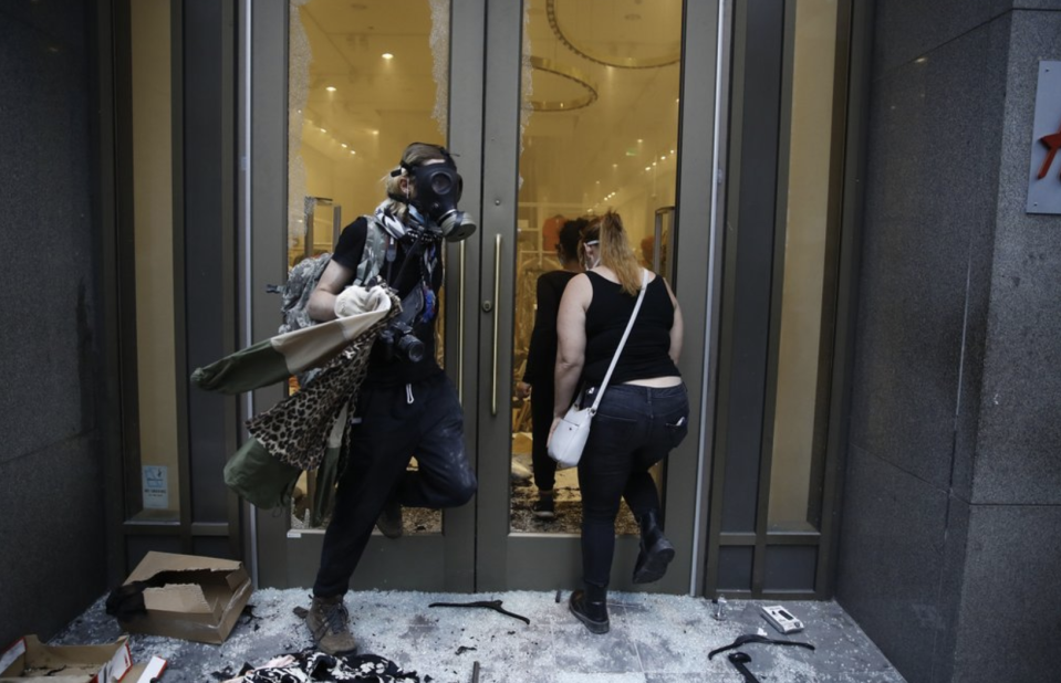 Pictured are two people at a smashed up H&M store in Philadelphia - one is wearing a mask.