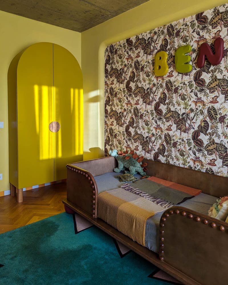 Yellow kids room with botanical wallpaper accent wall, brown leather and wood bed, and arch-shaped yellow wardrobe