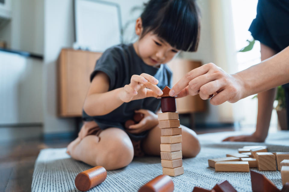 Close up of young Asian mother and little daughter having fun playing wooden building blocks together, enjoying mother and daughter bonding time at home. Learning through play concept