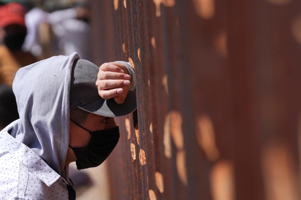 A young migrant looks through the border wall as migrants seeking asylum march through the streets of Nogales, Sonora, to protest Title 42, Border Patrol abuse against migrants, and lack of access to health care in Nogales. The protest on Monday, Sept. 26, 2022, followed the World Day of Migrants and Refugees.