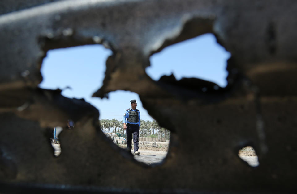 An Iraqi policeman, seen through broken fence, inspects the site of a car bomb explosion in Hillah, about 60 miles (95 kilometers) south of Baghdad, Iraq, Thursday, April 24, 2014. A suicide bomber rammed his explosives-laden car into a police checkpoint south of Baghdad on Thursday morning, killing several people, officials said, the latest episode in an uptick in violence in the run-up to next week's parliamentary elections. (AP Photo/Karim Kadim)