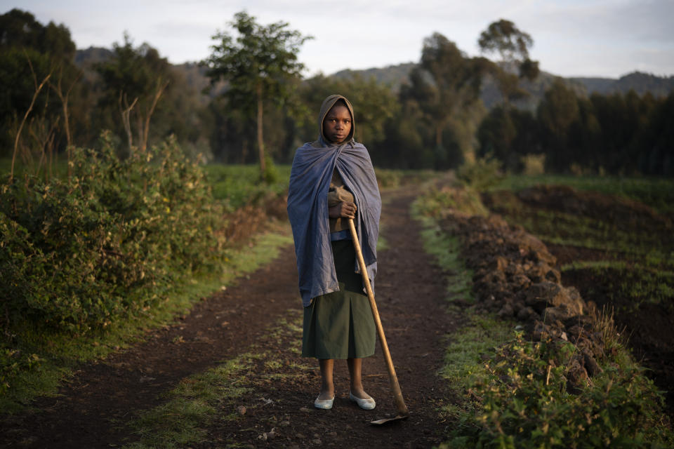 In this Sept. 5, 2019 photo, 13-year-old farmer Julienne poses for a photo in Kinigi, Rwanda. In 2005, the government adopted a model to steer 5% of tourism revenue from Volcanoes National Park to build infrastructure in surrounding villages, including schools and health clinics. Two years ago, the share was raised to 10%. (AP Photo/Felipe Dana)