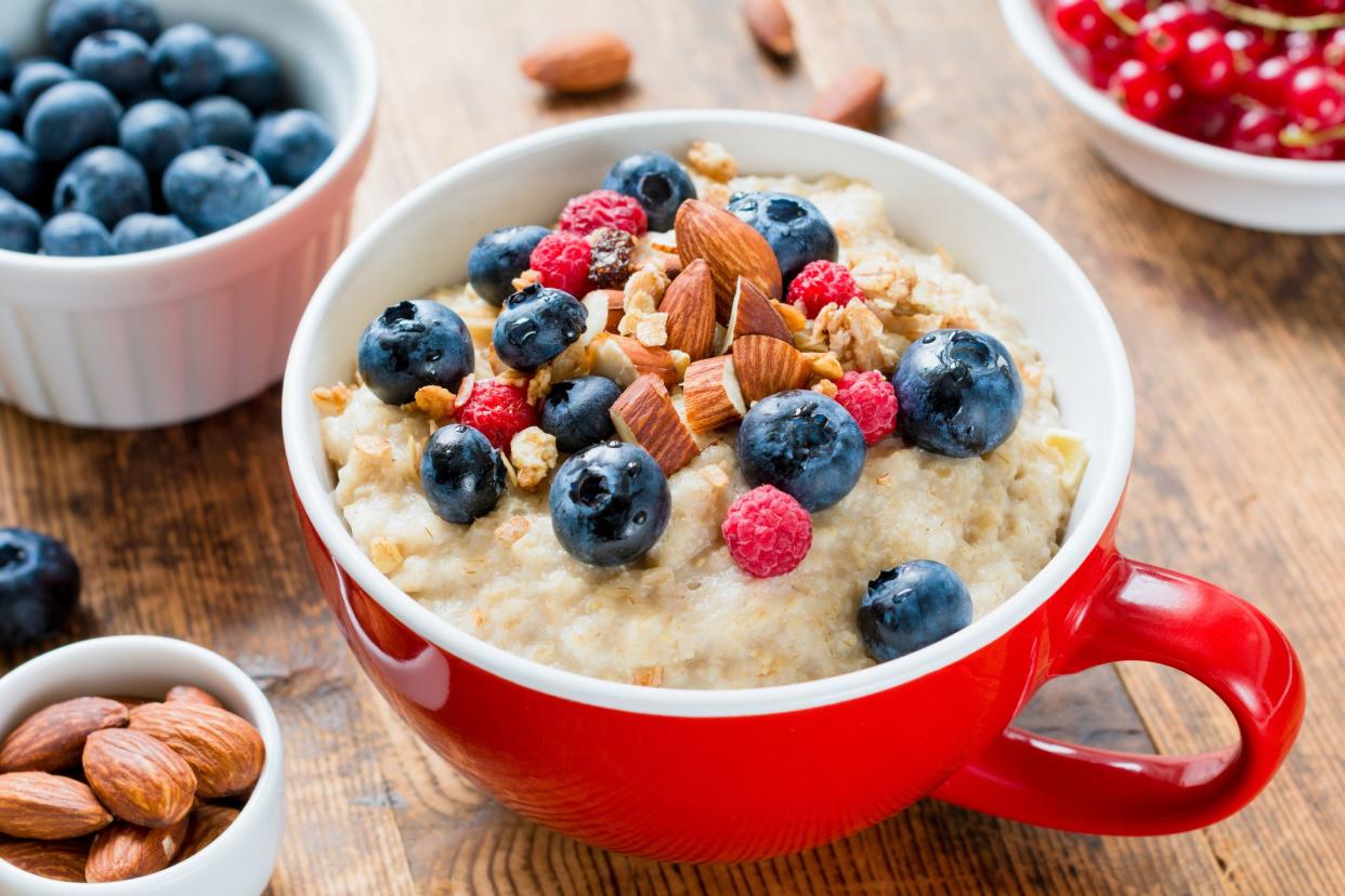 Close up view of delicious breakfast oatmeal porridge in red bowl topped with fresh blueberries, raspberries, almonds and granola.