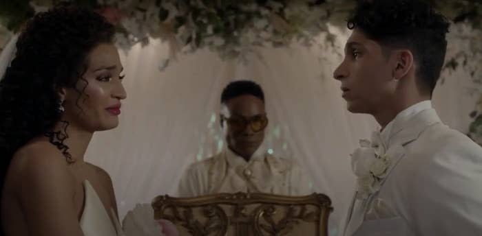 Three people at a wedding: Indya Moore in a sleeveless dress smiling at Angel Bismark Curiel in a suit, with Billy Porter officiating in an elaborate outfit