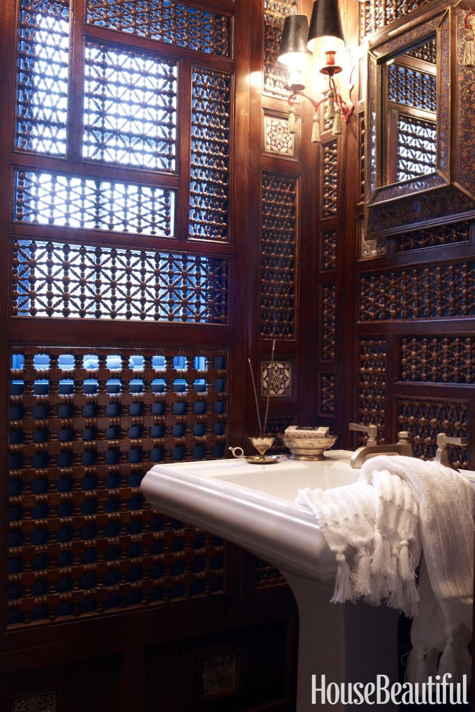 <p>A powder room behind a staircase embraces its tininess and becomes a moody, exotic jewel box with allover Moroccan fretwork. The perforated panels allow light to filter in while camouflaging less-than-perfect walls.</p>