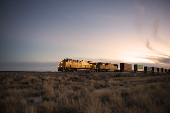 A train crossing a field as the sun sets behind it.