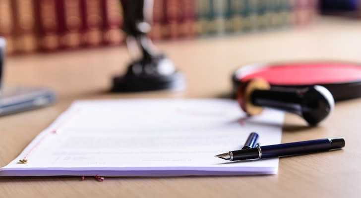 Image shows a stack of legal documents sitting on a table in a law office. SmartAsset identifies the differences between power of attorney and guardianship.