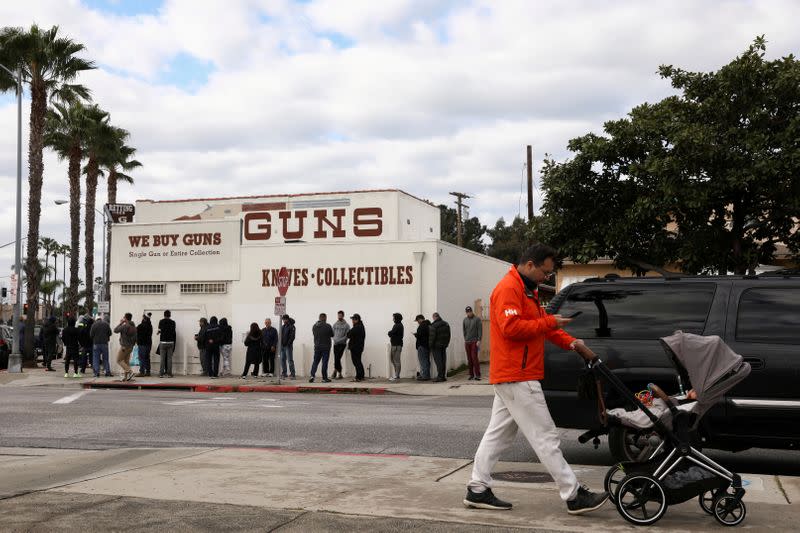 FILE PHOTO: A pedestrian pushes a stroller as people wait in line outside to buy supplies at the Martin B. Retting, Inc. gun store amid fears of the global growth of coronavirus cases, in Culver City