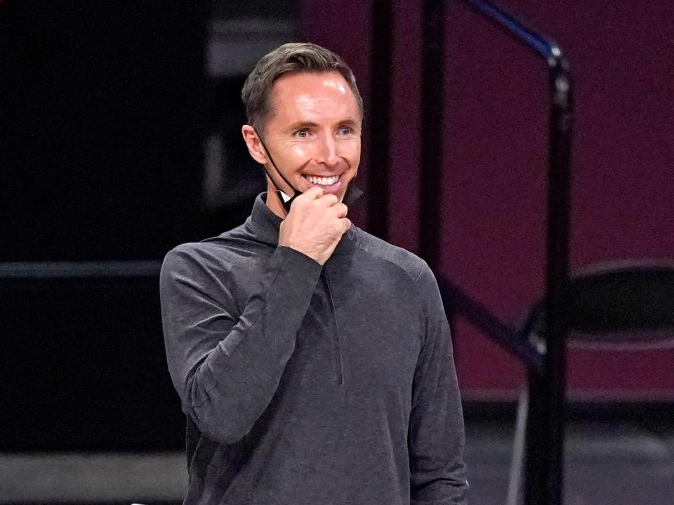 Steve Nash smiles while pulling his mask down on the sidelines of a Nets game in 2020.