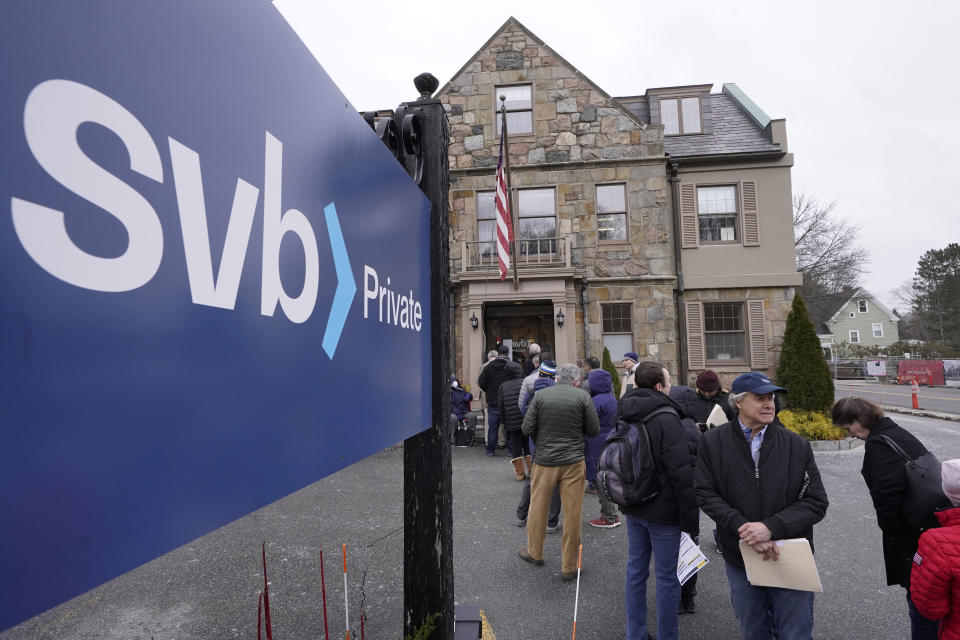 FILE - Customers and bystanders form a line outside a Silicon Valley Bank branch location, Monday, March 13, 2023, in Wellesley, Mass. The sudden crisis in the U.S. banking industry is sure to cause some tightening of lending and credit and a slowdown in the pace of borrowing and spending. If it does, the crisis could actually end up aiding the Federal Reserve in the elusive goal the Fed has been pursuing for a full year: A much lower inflation rate. (AP Photo/Steven Senne, File)