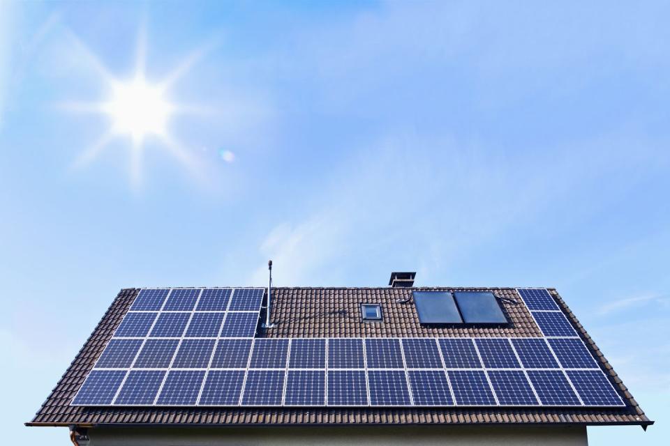 Germany, Solar panels on houseroof in front of blue sky with sun