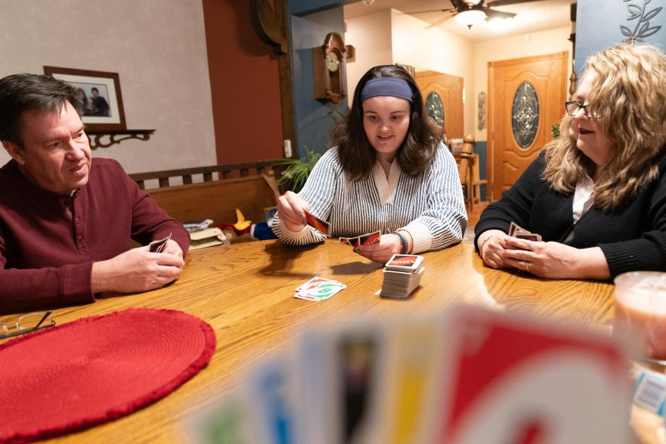 Sheridan Elskamp, middle, places down a green reverse card while playing UNO with her parents, Rick Elskamp, left, and Anna Elskamp, right, Thursday evening at their home in Tecumseh. The family was recently notified they were finally removed from the Intellectual and Developmental Disability Waitlist after a decade of waiting to recieve aid for Sheridan.